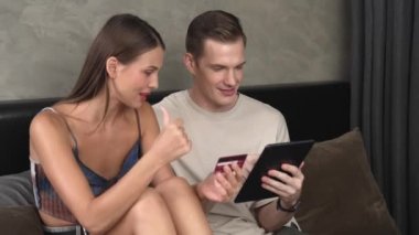 Genç çift, kredi kartıyla ödeme yapabilmek için internet üzerinden ödeme uygulaması ve dijital cüzdan kullanarak yatak odasında oturuyor. Mobil internet üzerinden alışveriş ve modern alımlar. Düzenle