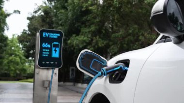 Doğal yeşil araba parkındaki ekolojik temiz enerji şarj istasyonundan gelen fütürist akıllı EV şarj aletinin şarj ettiği elektrikli araba. Alternatif enerji kullanan gelecekçi çevre dostu elektrikli araba. İnceleyin