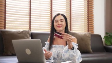 Genç bir kadın internet bankacılığı için kredi kartıyla dizüstü bilgisayar kullanıyor. Evinde online ödeme kapısı ile E ticareti yapıyor. Banka kartıyla modern ve kullanışlı online satın alma. Blithe