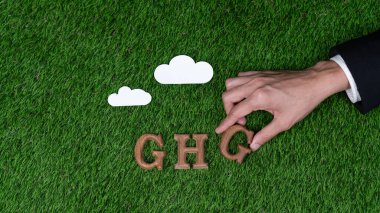 Sera azaltma kampanyası ve çevresel farkındalık mesajını teşvik etmek için eko sembolü olarak sera gazları simgesi olan biyofilik arkaplan üzerine GHG 'deki ahşap alfabe metnini elle düzenleyin. Döngü