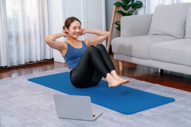 Spor kıyafetli Asyalı bir kadın antrenman rutini olarak spor minderini çıtırdatıyor. Çekici kız sağlıklı yaşam tarzını online egzersiz videosuyla takip ediyor. Kuvvetli