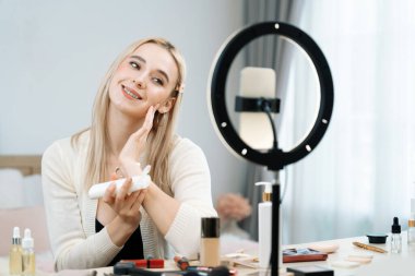 Sosyal medya için güzellik ve kozmetik video içeriği hazırlayan genç bir kadın. Güzellik blogcusu kameraya gülümserken seyirciye ya da takipçilere güzellik teninin nasıl uygulanacağını gösteriyor. Blithe