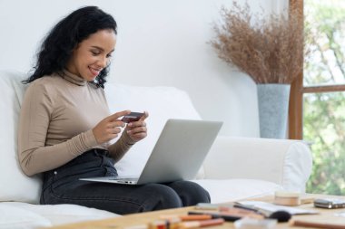 Genç mutlu bir kadın internetten alışveriş yaparak ürün satın alırken aynı zamanda internet üzerinden online kredi kartı ödeme sistemi ile çevrimiçi mağaza platformundan önemli siber güvenlik tarafından korunan ürünler sipariş ediyor.