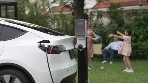 幸せで遊び心のある家族が一緒に遊ぶ背景にある家庭用充電ステーションからの電気自動車の充電 より良い未来のFastidiousのための代替および持続可能なエネルギーを使用するEv車 — ストック動画