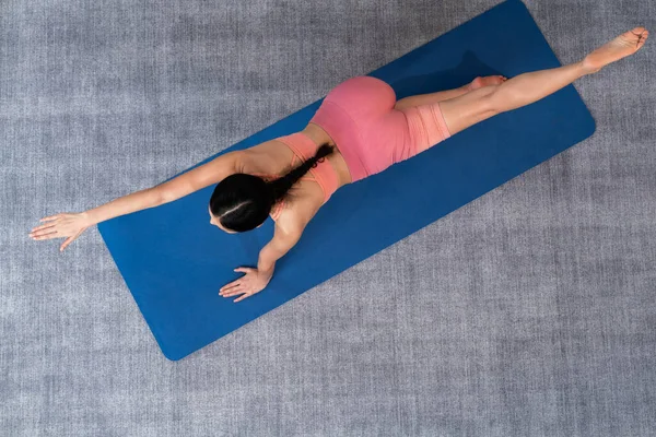 Top view asian woman in sportswear doing yoga exercise on fitness mat as her home workout training routine. Healthy body care and calm meditation in yoga lifestyle. Vigorous