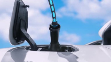 Elektrikli şarj için elektrikli arabaya EV şarj prizi takın. Elektrik şarj istasyonu tarafından, gökyüzünün altında parlayan ışık hologramıyla yakın çekim yapın. Geleceğin yeniliği ve enerji sürdürülebilirliği. İncelenme