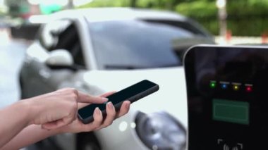 Modern iş kadını akıllı telefonun 3D hologramından batarya durumunu kontrol ederken EV arabasının şarj olan enerjisini kontrol eder. Gelecekteki EV otomotiv teknolojisinin yenilikçi teknolojik gelişimi. İnceleyin