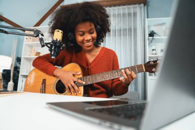 Genç Afrikalı Amerikalı müzisyenin sunucu kanalı gitar çalıyor, şarkı söylüyor, stüdyoda dizüstü bilgisayardan yayın yapıyor. Kulaklık dekorasyonu ve mikrofon kaydı. Tatlandırıcı.