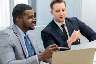 Afrikalı erkek lider stratejiyi açıklarken profesyonel proje yöneticisine çözümünü dizüstü bilgisayar kullanarak belgeye işaret ederek gösteriyor. Yetenekli iş adamlarının beyin fırtınası fikri. İş toplantısı. Süslü.
