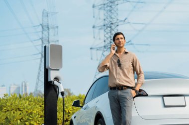 Şarj istasyonundaki EV araba aküsünü şarj ederken konuşan adam elektrik şebekesine bağlı elektrik endüstrisi çevre dostu araba kullanımı için elektrik endüstrisi.