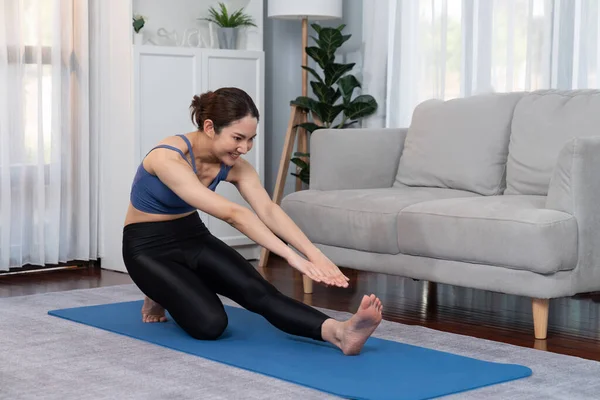 stock image Asian woman in sportswear doing yoga exercise on fitness mat as her home workout training routine. Healthy body care and calm meditation in yoga lifestyle with comfortable and relaxation. Vigorous