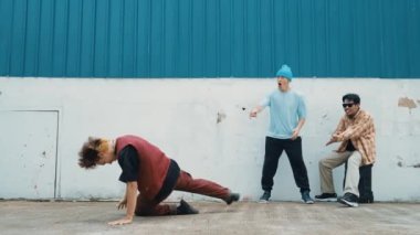 Genç Asyalı dansçı hip hop tarzında dans ediyor ve çok kültürlü arkadaşları duvarın arkasında tezahürat yapıyor. Çekici yakışıklı adam mavi arka planda kollarını uzatıyor. Açık hava sporu 2024 hiphop..
