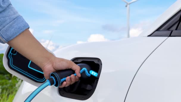 亚洲人通过风力涡轮机将智能电动汽车充电器插入电动汽车 利用电动汽车进行可持续清洁运输的未来可再生能源利用 仔细阅读 — 图库视频影像
