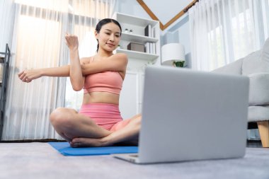 Spor kıyafetli Asyalı bir kadın spor salonunda antrenman yaparken spor minderinde yoga yapıyor. Sağlıklı vücut bakımı kadın dizüstü bilgisayardan yoga videosu izliyor. Kuvvetli