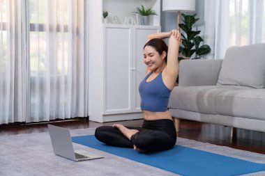 Spor kıyafetli Asyalı bir kadın spor salonunda antrenman yaparken spor minderinde yoga yapıyor. Sağlıklı vücut bakımı kadın dizüstü bilgisayardan yoga videosu izliyor. Kuvvetli