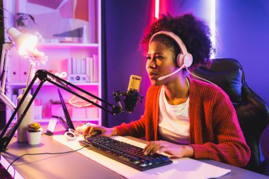 Neon renkli aydınlatma odasında kulaklık takan Afrika kökenli Amerikalı kız flamalı Esport yetenekli takımıyla online dövüş yapıyor. Rakiplerini kazanmak için strateji planlayan diğer oyuncularla konuşmak. Tatlandırıcı.