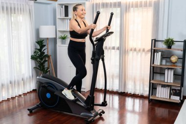 Emeklilerin emekliliğinden sonra sağlıklı bir yaşam tarzı ve vücut bakımı olarak ev portresi çekilen eliptik koşu makinesinde çalışan aktif son sınıf öğrencisi bir kadın. Etki