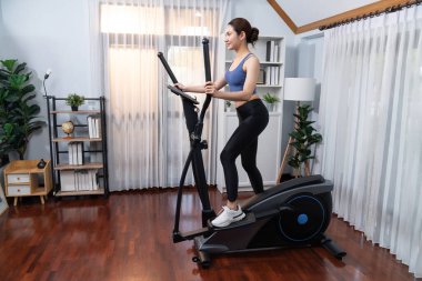 Enerjik ve güçlü atletik Asyalı kadın evde eliptik koşu makinesiyle koşuyor. Formda fiziğin takibi ve ev çalışması ve eğitimle sağlıklı yaşam tarzına bağlılık. Kuvvetli