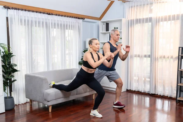 Active and fit senior couple warmup and stretching using furniture before home exercising routine at living room. Healthy fitness lifestyle concept after retirement for pensioner. Clout