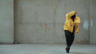 Hippi sokak, şehir merkezinde ayak izleri gösteriyor ya da pratik yapıyor. Break dansçının hareket halindeyken kulaklıktan müzik dinlediği sahne. Açık hava sporu 2024. Gri arka plan. Hip hop modası. hiphop.