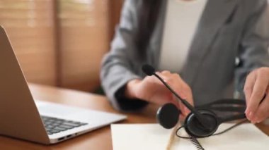 Kadın çağrı merkezi operatörü ya da müşteri hizmetleri çalışanı, müşteriye yardım etmek için kulaklıkla konuşurken çalışma alanı üzerinde çalışıyor. Profesyonel modern iş hizmeti. Blithe