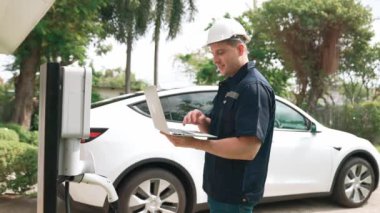Evde EV şarj istasyonu kurulumu üzerinde çalışan nitelikli teknisyen, EV için dizüstü bilgisayarla şarj sisteminde sorun çıkarma ve yapılandırma ayarları yapıyor. Titiz
