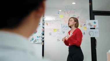 Yetenekli genç ve güzel iş kadını, yaratıcı iş toplantısında yakışıklı yönetici dinlerken zihin haritalama ve istatistiksel grafik kullanarak pazarlama fikrini kendine güvenle sunuyor. Tertemiz..