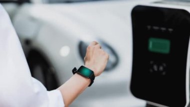 İş adamı, istasyonun otoparkından şarj olurken akıllı telefon hologramındaki EV aküsünün durumunu kontrol ediyor. EV teknolojisi adaptasyonu için temiz enerjinin gelecekteki yaşam tarzı. İnceleyin