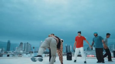 Profesyonel hippi hareketsiz poz verirken aynı zamanda şehir manzaralı çatıdaki müziğe ayak basıyor. Break dansçı, hip-hop dansçıları grubuyla birlikte sokak dansı yapıyor. Açık hava sporu 2024 hiphop..