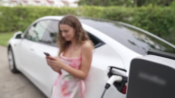 现代环保妇女从家用电动汽车充电站为电动汽车充电 创新的电动汽车技术用于跟踪能源使用情况 以优化国内的电池充电 太奇怪了 — 图库视频影像