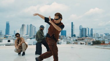 Bir grup profesyonel hip hop dansçısı çatıda break dans yapıyor. Becerikli koreograf serbest stil hareketini gösterirken, arkadaş da cesaretlendirir, alkışlar, alkışlar. Açık hava sporu 2024. ÇalışmaComment.