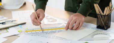 Planı ölçen profesyonel bir mühendis. Stüdyoda, sarı kasklı ve mimari teçhizatlı bir masada mimarlık projesinde çalışan profesyonel bir mühendis. Tanımlama.