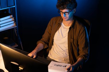 Genç işadamı, Neon Light Modern Ofis 'teki yeni proje surround çalışma masası için kağıt üzerinde tasarım düşünüyor. E-posta ile hediye göndermeden önce not defterine yeni bir iş düşünüyorum. Toplayıcı.