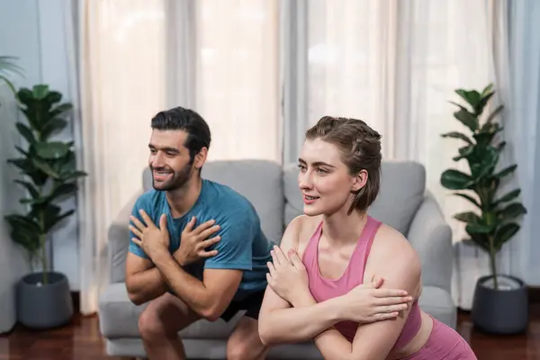 stock image Athletic and sporty couple doing squat together during home body workout exercise session for fit physique and healthy sport lifestyle at home. Gaiety home exercise workout training concept.