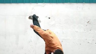 İspanyol adam kollarını uzattı ve duvarın önünde break dans yaptı. Hip hop tarzında dans eden günlük kıyafetli şık sokak dansçısının yakın çekimi. Açık hava sporu 2024. Geçmişi. hiphop.