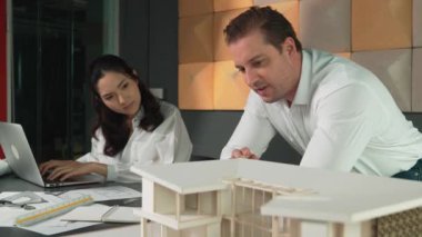Ev planı çizmek için birlikte çalışan yetenekli mimar mühendisi. Mimar takımı, mimari model, plan ve dizüstü bilgisayarla ofis masasına yerleştirilen ev inşaatı hakkında tartışır. Yönlendirici.