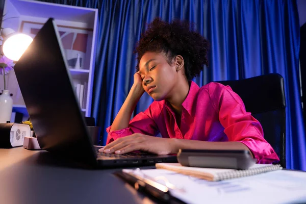 African woman freelancer feeling tried and take a nap on desk around by laptop and stationary, waiting for proceed project job until sleeping on desk. Concept of work life at home place. Tastemaker.