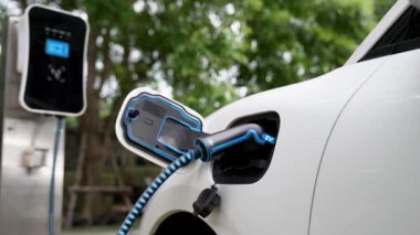 Doğal yeşil araba parkındaki ekolojik temiz enerji şarj istasyonundan gelen fütürist akıllı EV şarj aletinin şarj ettiği elektrikli araba. Alternatif enerji kullanan gelecekçi çevre dostu elektrikli araba. İnceleyin