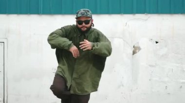 Sokak ortasında mavi duvarlı hippi dansçı ayak basamağı. Asyalı break dansçı kollarını açarken sokak dansı yapıyor. Hip hop koreografı enerjik bir dans sergiliyor. Açık hava sporu 2024 hiphop..