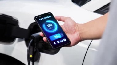 Akıllı telefon ekranı akıllı EV mobil uygulama üzerinde pil durumu EV araba garajdaki ev şarj istasyonu ile elektrik şarj ederken. Geleceğin yenilikçi EV arabası ve enerji sürdürülebilirliği. İnceleyin