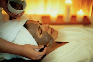 Kaplıca salonunun sakin atmosferi, kadın müşteri sıcak mum ve kömür kömürü yüz kremi masajıyla kendini yenileme zevkine kapılıyor. Yüz bakımı ve güzellik konsepti. Sessiz.