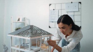 Genç, güzel ve zeki mühendisin yakın çekimleri modern ofiste duvarında taslak olan kalem kullanarak ev modelini ölçmeye odaklanıyor. Yaratıcı yaşam ve tasarım konsepti. Tertemiz..