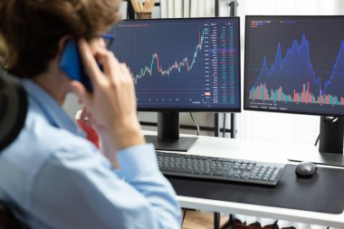 Genç yatırımcı borsa simsarı akıllı telefondan borsacıya arıyor, modern ofiste mevcut pazar grafiğindeki iki dizüstü bilgisayardaki dinamik finansal değişim yatırımını tartışıyor. Toplayıcı.