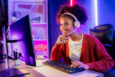 Neon renkli aydınlatma odasında kulaklık takan Afrika kökenli Amerikalı kız flamalı Esport yetenekli takımıyla online dövüş yapıyor. Rakiplerini kazanmak için strateji planlayan diğer oyuncularla konuşmak. Tatlandırıcı.