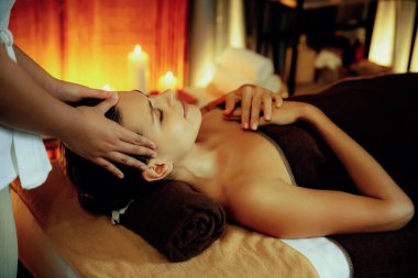 Beyaz kadın stres önleyici kafa masajı yapmaktan ve lüks otel veya otelde sıcak mum ışığında yüz güzelliği eğlencesi yapmaktan zevk alıyor. Sessiz.