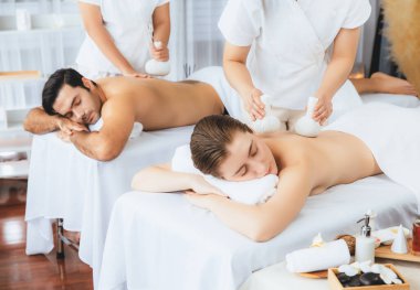 Sıcak bitkisel top spa masaj vücut tedavisi, masör nazikçe bitki torbasını çift müşteri vücuduna bastırıyor. Aromaterapi dinlenme sükuneti ve sükuneti kaplıca salonundaki atmosferi aydınlatıyor. Sessiz.