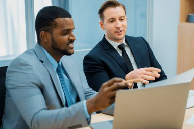 Afrikalı erkek lider stratejiyi açıklarken profesyonel proje yöneticisine çözümünü dizüstü bilgisayar kullanarak belgeye işaret ederek gösteriyor. Yetenekli iş adamlarının beyin fırtınası fikri. İş toplantısı. Süslü.