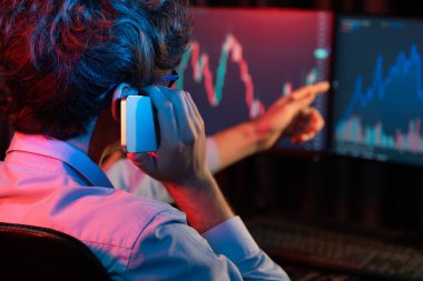 Akıllı telefondan borsaya tartışan genç yatırımcı, modern ofiste mevcut pazar grafiğindeki iki dizüstü bilgisayarda dinamik mali değişim yatırımına işaret ediyor. Toplayıcı.