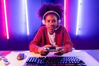 Oyun flamasının sunucu kanalı, joystick ile online oyun oynayan Afrikalı kız, mikrofondan izleyici medyasıyla konuşuyor. Esport yetenekli takım oyuncuları neon renkli aydınlatma odasında. Tatlandırıcı.