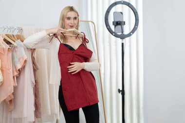 Genç sosyal medyum kadın moda videosu yapıyor. Blogcu kameraya ve ışık çemberine gülümserken, aynı zamanda ikna edici çevrimiçi kıyafetleri izleyicilere veya takipçilere vlog sattırıyor. Blithe